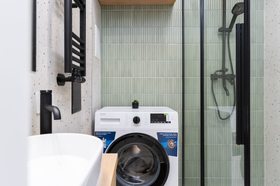 Compact washer in a small modern bathroom beside a shower and sink.