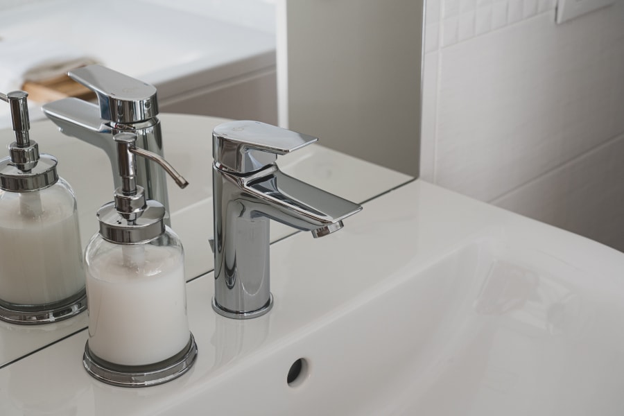 Chrome bathroom sink faucet with two glass soap dispensers on a white countertop
