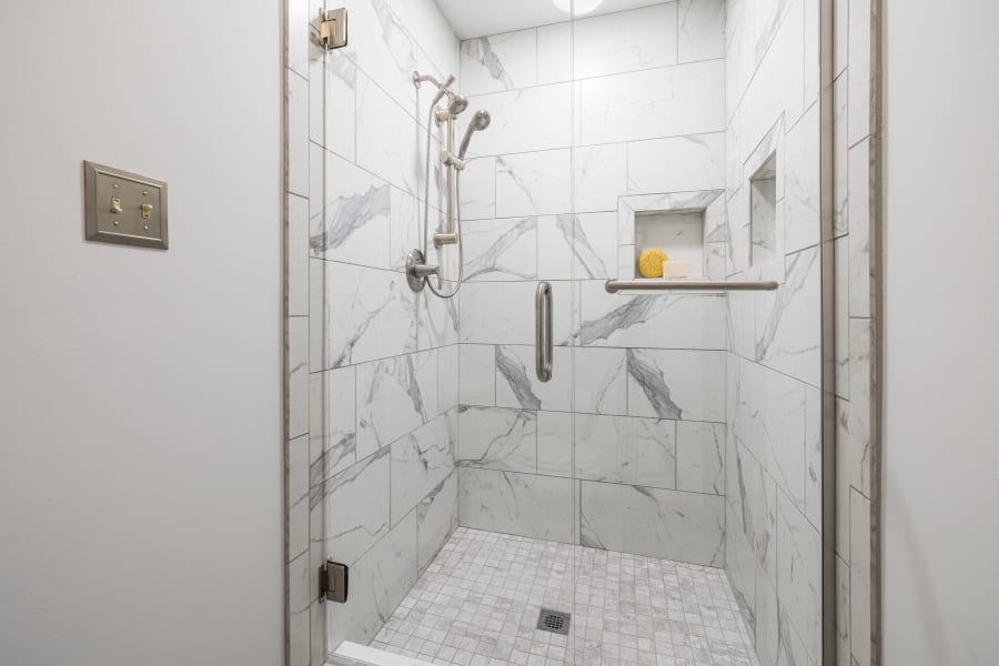 Marble-tiled walk-in shower with glass door, chrome fixtures, and built-in shelf with soap