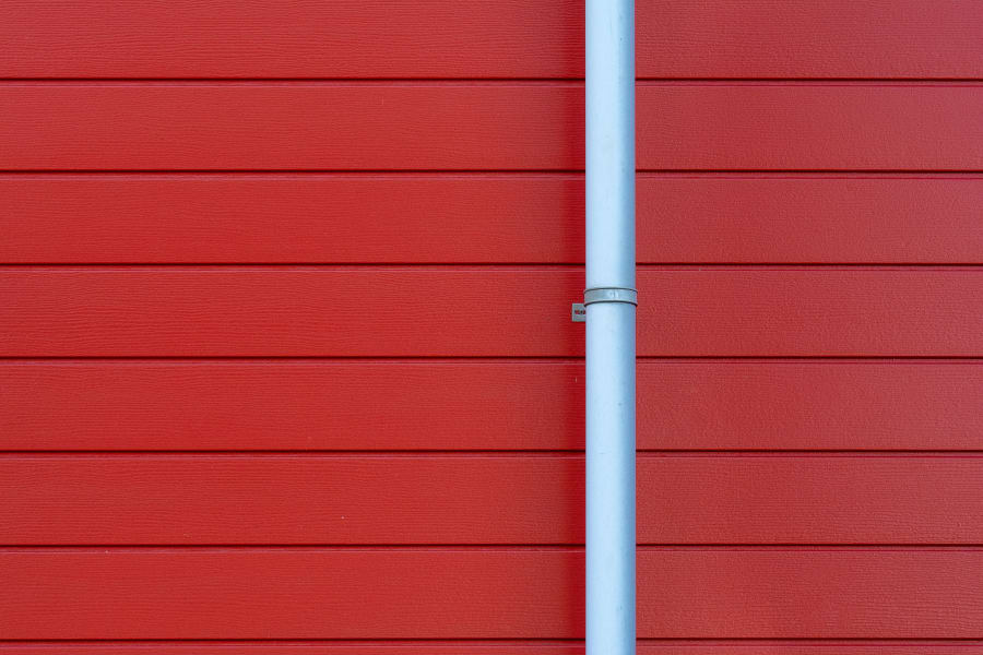 Red wooden wall with a vertical light gray pipe in the center