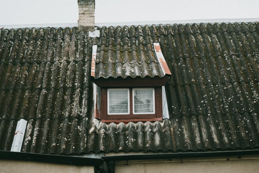 Dormer window on a weathered tiled roof with a chimney in the background