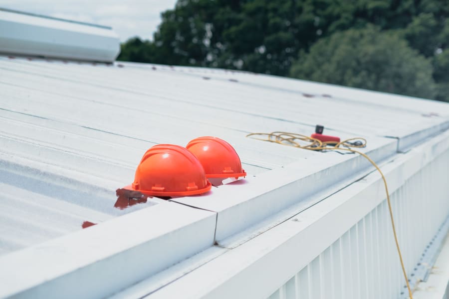 Two orange hard hats on a white rooftop beside safety gear and a rope line.
