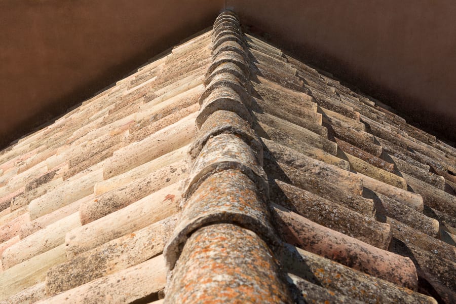 Close-up of a weathered tiled roof ridge against a brown wall corner