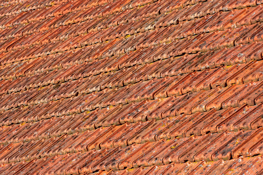 Close-up of a reddish-orange tiled roof with diagonal ridges and weathered texture