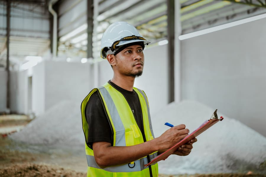 Construction worker in hard hat and reflective vest taking notes at an industrial site