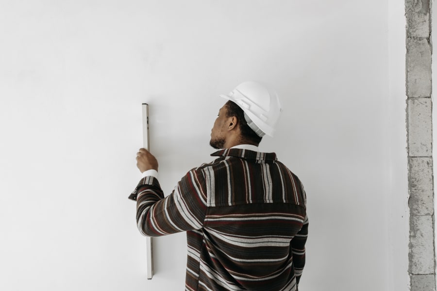 Person in a hard hat measuring a white wall with a level at a construction site.