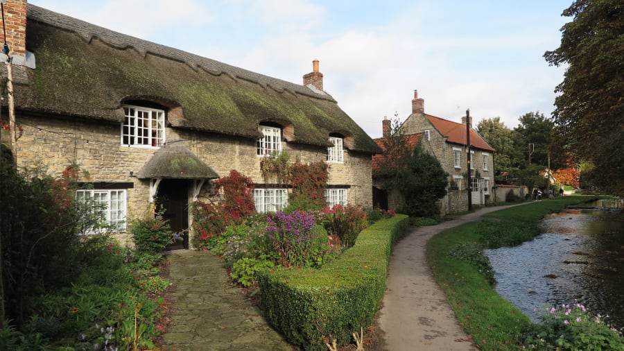 Thatched cottages beside a winding riverside path and stream in a quaint village