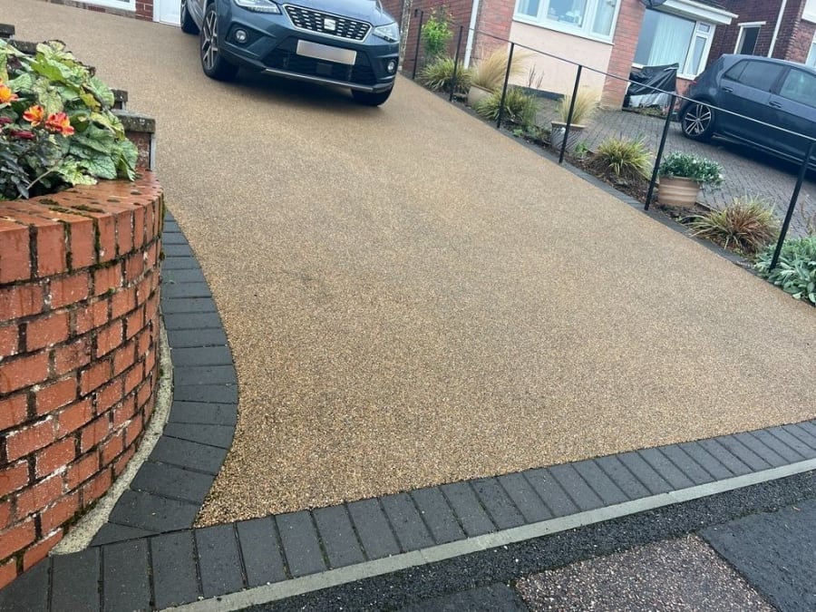 Brown resin driveway with block paving border, sloping downhill