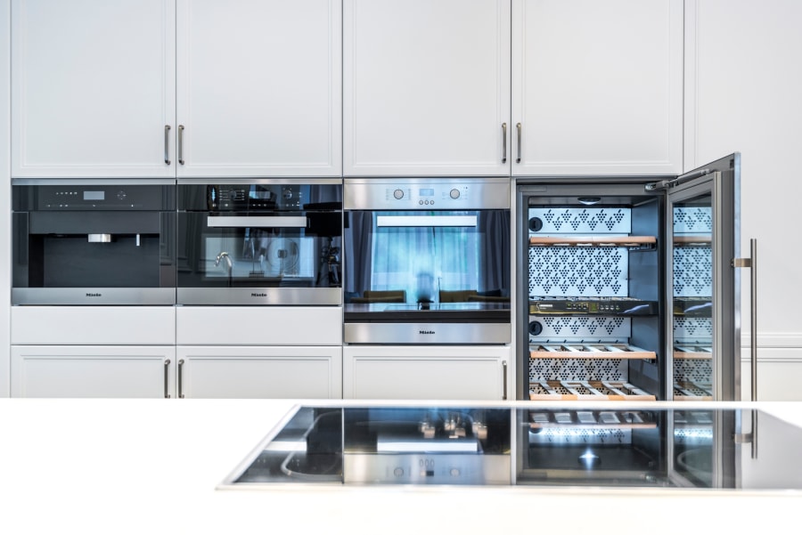 Modern white kitchen with built-in ovens and a glass-door wine cooler in a wall of cabinetry