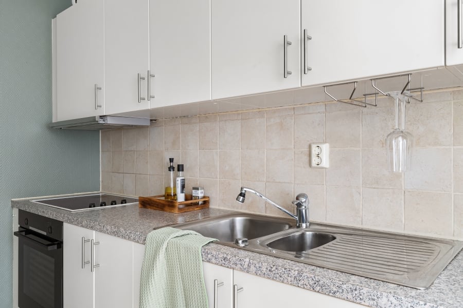 Modern kitchen counter with white cabinets, stainless sink, stovetop, and a towel draped over the counter