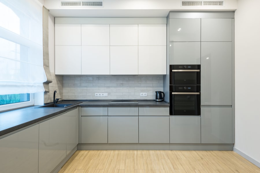 Modern minimalist kitchen with gray cabinets, white upper cupboards, black countertop, and wood floor.