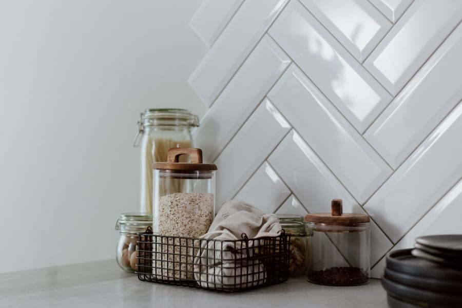 Glass jars and canisters on a kitchen counter against a white herringbone tile backsplash
