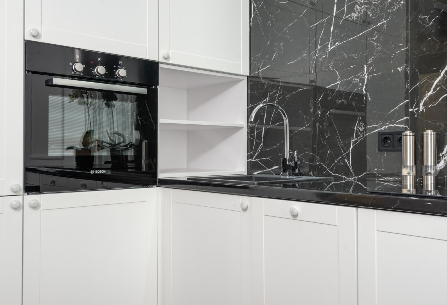 Modern white kitchen with black marble backsplash, built-in oven, and stainless sink