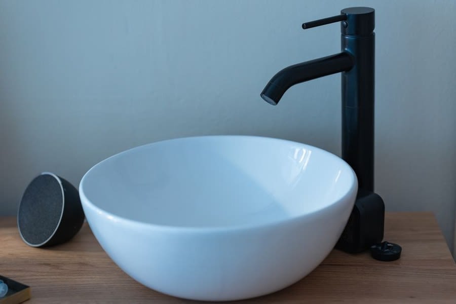 Round white counter-top basin with a matt black pillar tap on a timber surface