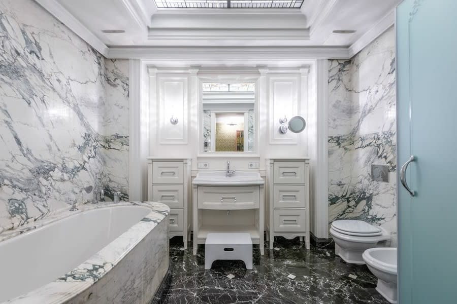 Renovated bathroom with veined marble walls and classic painted vanity units
