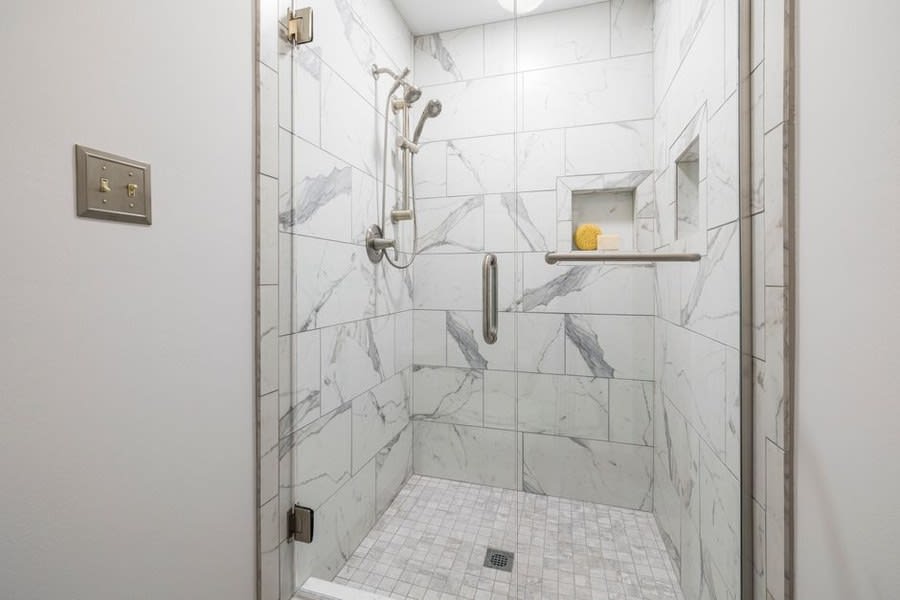Marble-tiled shower enclosure with a recessed shelf and glass screen