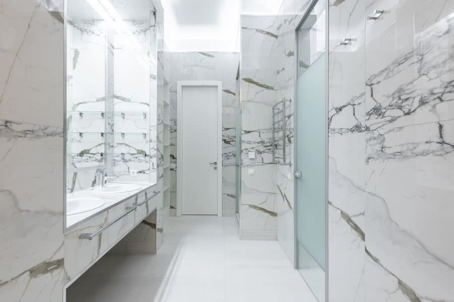 Marble-lined bathroom with a walk-through shower and long vanity mirror