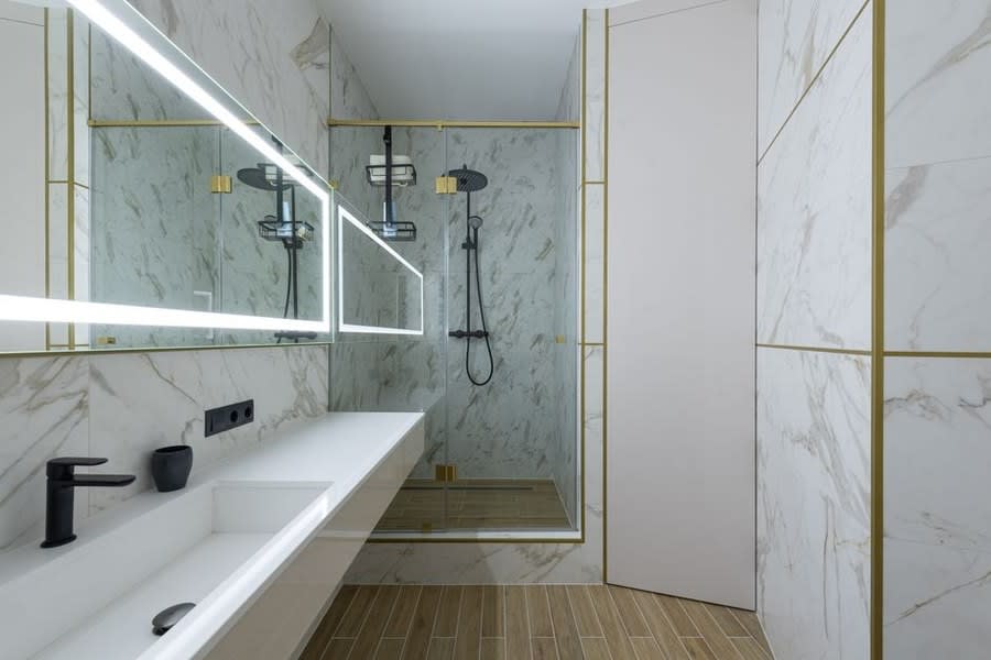 White marble walk-in shower with slim gold inlay detailing and a linear drain