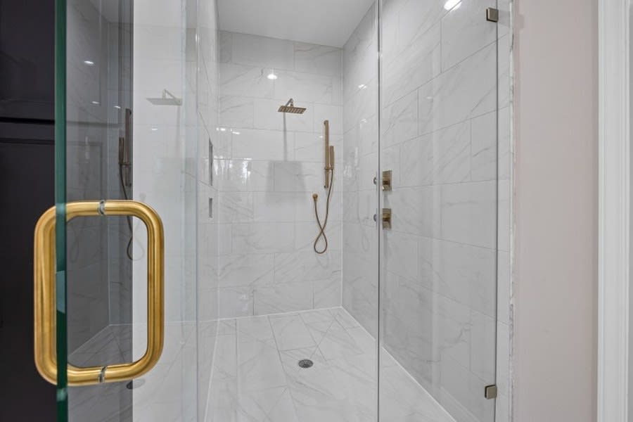 Brass shower door handle on a frameless marble-lined walk-in shower