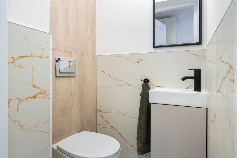 Small modern bathroom with marble walls, white sink, black faucet, and a toilet beside a wooden panel.