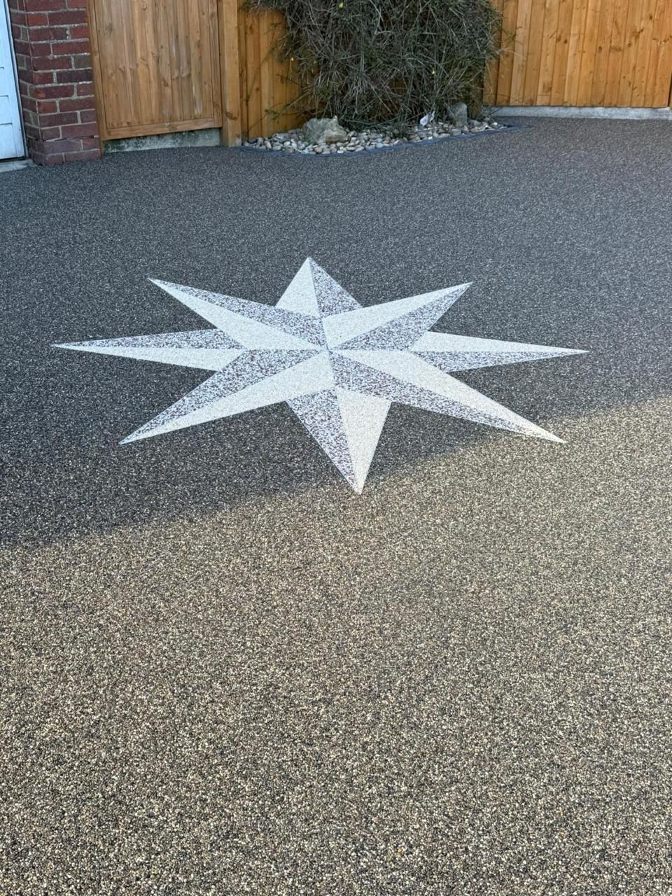 A white compass rose design inlaid into a textured, dark gray gravel driveway.