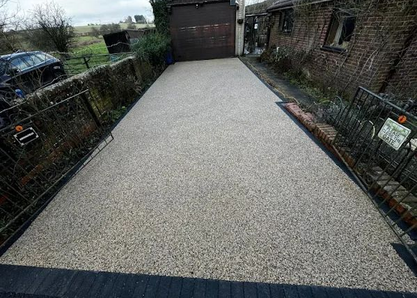 Gravel driveway bordered by brick walls, leading to a garage at the end.