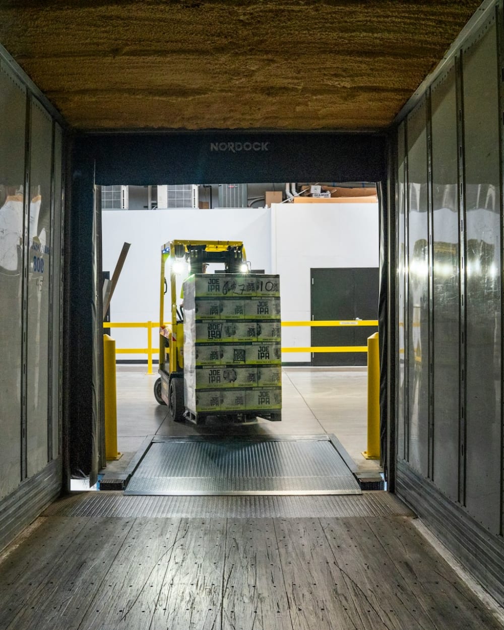 A forklift carrying a stacked pallet through a warehouse loading dock