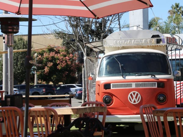 Vintage red and white VW van bar with striped umbrellas and patio seating in San Diego