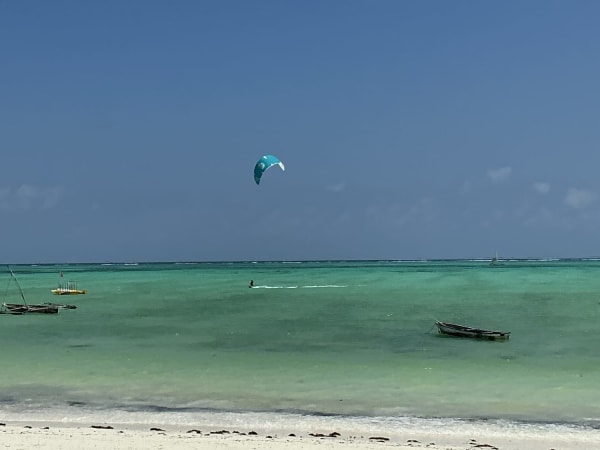 Kitesurfer airborne over shallow turquoise water with wooden boats moored near Zanzibar beach