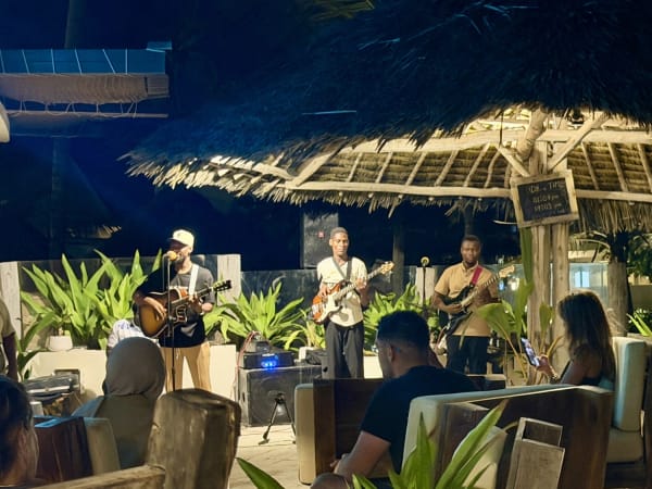 Three musicians performing under thatched roof at Zanzibar open-air venue at night