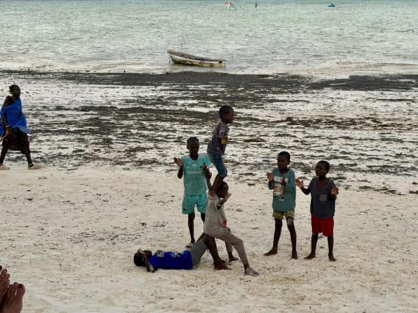 Children playing on white sand beach in Zanzibar with wooden fishing boats at low tide