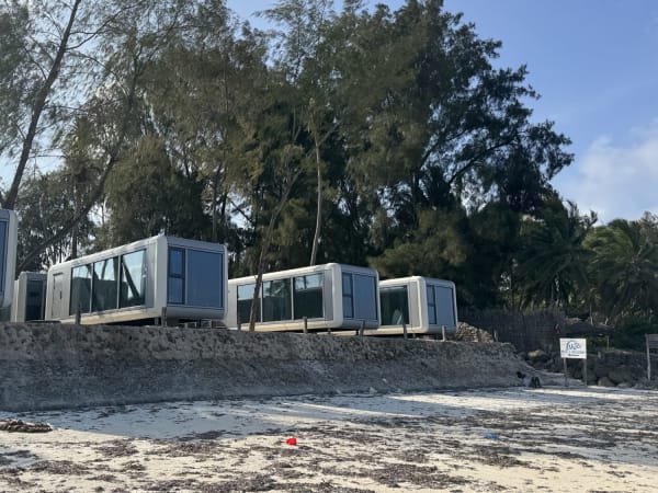 Prefabricated cabin units on stilts along sandy Zanzibar beach with casuarina and palm trees