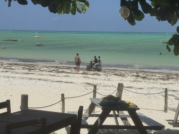 White sand beach in Zanzibar with turquoise water, anchored boats, and shaded picnic seating