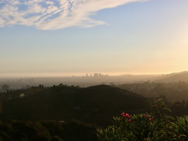 Sunset over city buildings and hillsides with vegetation near Griffith Observatory.