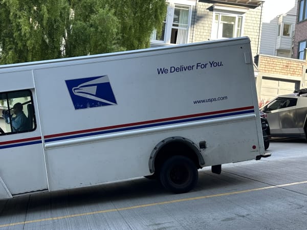 USPS mail truck on San Francisco residential street with weeping trees and parked cars