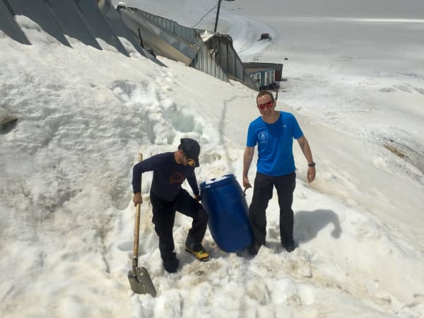 Two expedition members handling blue barrel on snow slope, Mount Elbrus Expedition
