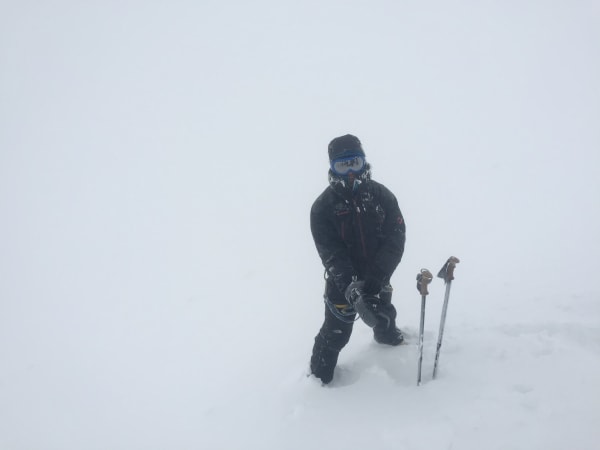 Mountaineer in full gear kneeling in deep snow during Mount Elbrus Expedition