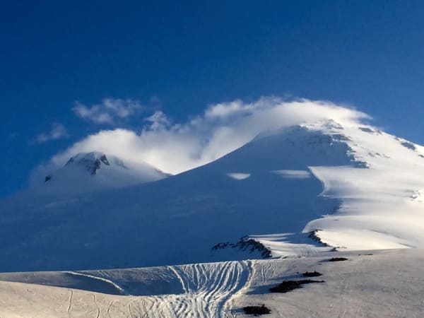 Twin-peaked snow mountain with wind clouds and boot tracks, Mount Elbrus Expedition