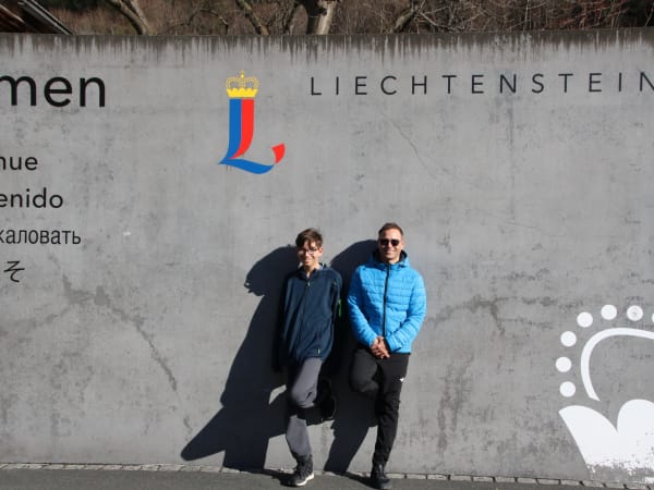 Two people standing before a concrete Liechtenstein welcome wall in Vaduz