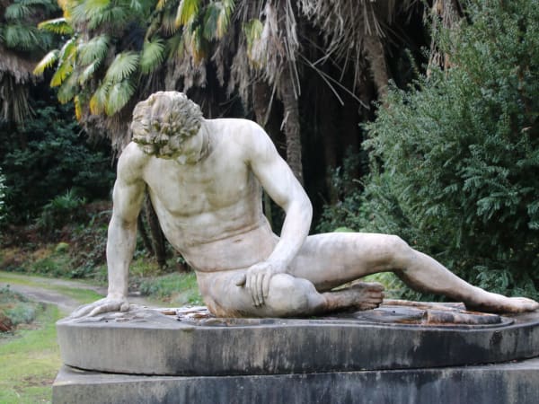 White marble reclining male sculpture on stone pedestal in Verbania garden