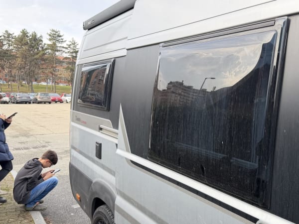 White campervan parked in open lot in Turin, two people nearby