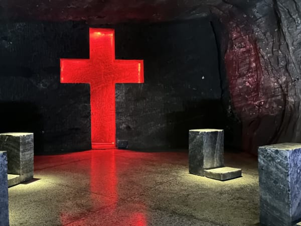 Red illuminated cross carved into dark rock wall with stone seats at Zipaquirá – Catedral de Sal