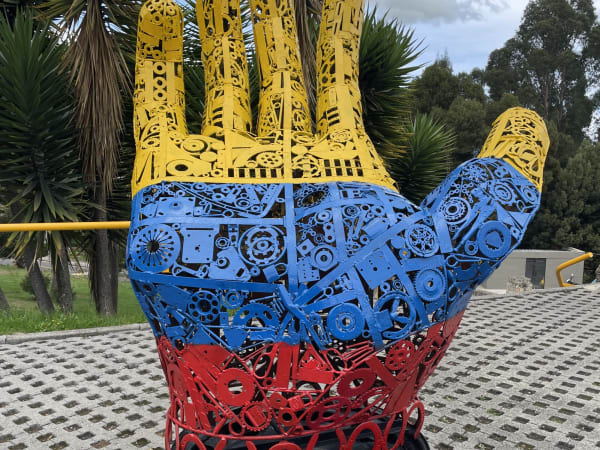 Metal hand sculpture with yellow, blue, and red bands on paved plaza, Zipaquirá – Catedral de Sal