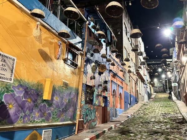 Cobblestone alley at night with painted facades and suspended wicker baskets in La Candelaria