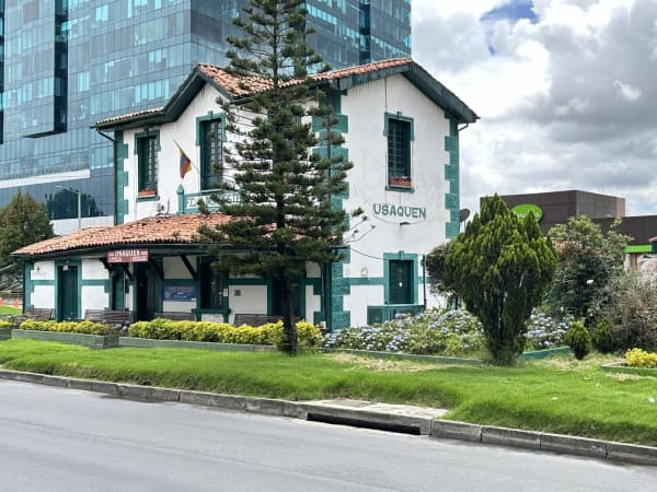 Historic white building with teal trim and terracotta roof in La Candelaria, Colombia, with modern glass tower behind