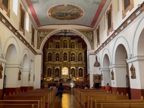 Colonial baroque church nave with gilded altarpiece and wooden pews in La Candelaria