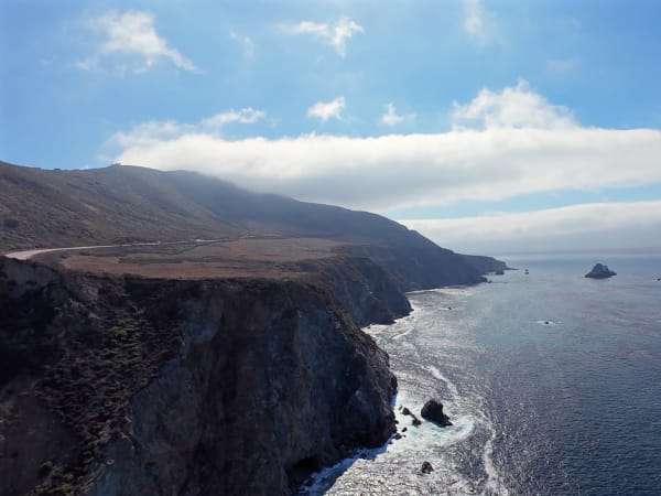 Rocky Big Sur coastline with offshore formations, cliffs, ocean water, and narrow hillside road