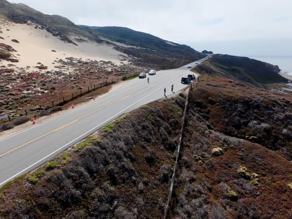 Two-lane coastal highway with traffic cones, vehicles, and ocean bluffs in Big Sur