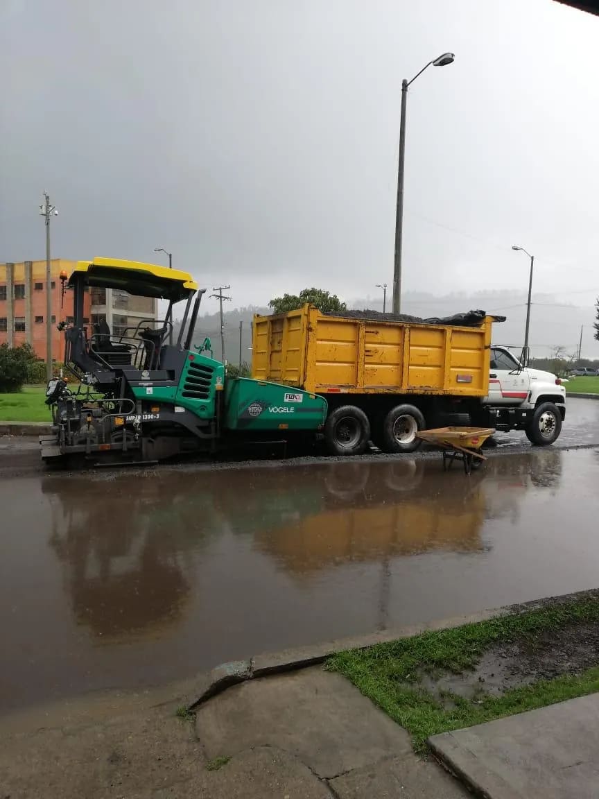 Pavimentadora extendiendo asfalto en frío descargado de la volqueta.
