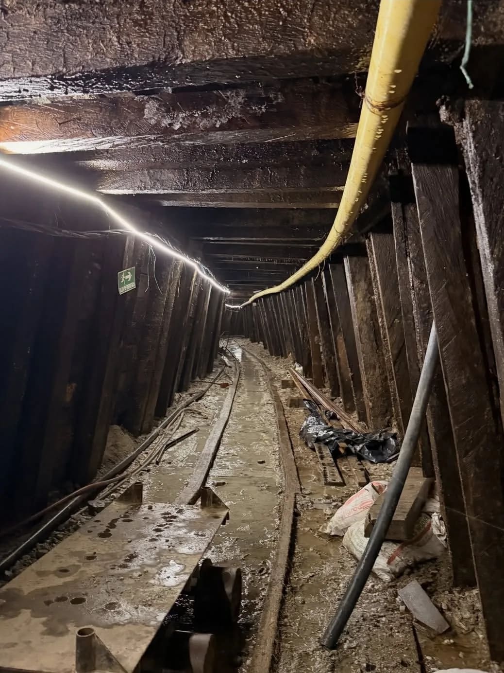 Interior de socavón con entibado en madera y rieles de transporte.